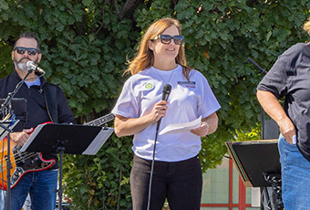 Kelly Milne speaking on stage with a band behind her.